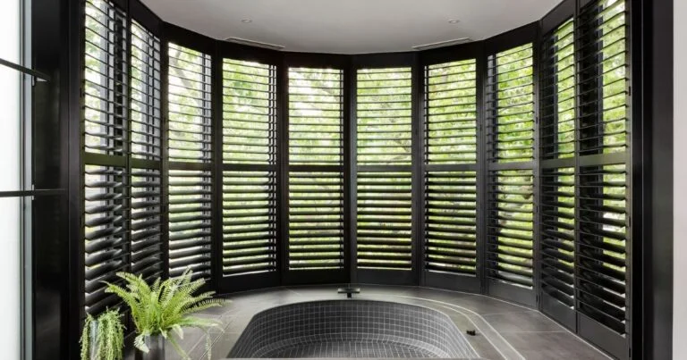 Shutters - Beanstalk Mums Curved wall of black shutters with greenery visible outside and a small circular tiled hot tub in a modern spa room.