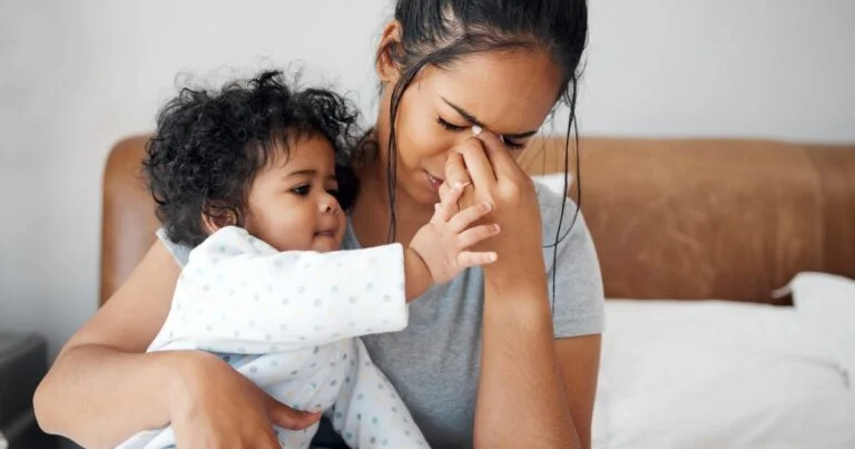 Sick mum survival guide - Beanstalk Mums Mother and baby cuddling on a bed; baby reaches to touch mother's face with a gentle expression of connection and care.