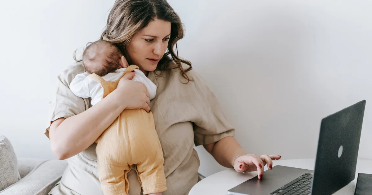 TPD cover - Beanstalk Mums Mother cradling a baby while using a laptop at a white table in a home setting. (informative image)